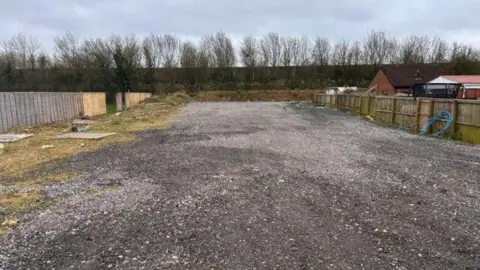 Somerset Council An empty area of the site which has a wide path covered in gravel. There are fences on the side where some of the residential pitches are.