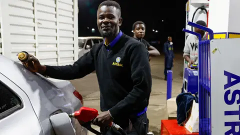 A pump attendant, in a black sweater written Astrol fuels a car at an petrol station in Kenya