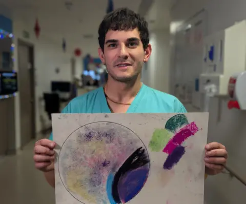 Dr Francesco Rosato, who has dark hair and is holding up his artwork