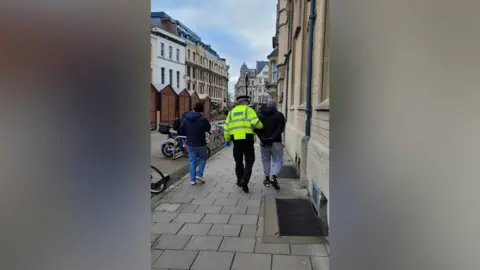 Thames Valley Police A man is led away wearing handcuffs by a uniformed officer