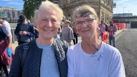 The two women smile for the camera, one has dirt on her face from helping clean up