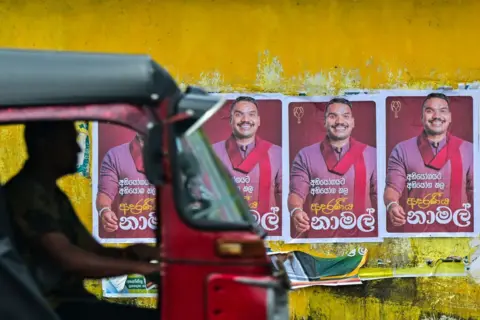 Een rode motortaxi passeert een gele muur met posters van een man met een rode sjaal