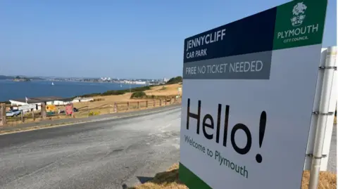 A close up picture of a Jennycliff car park sign taken on a bright sunny day. 