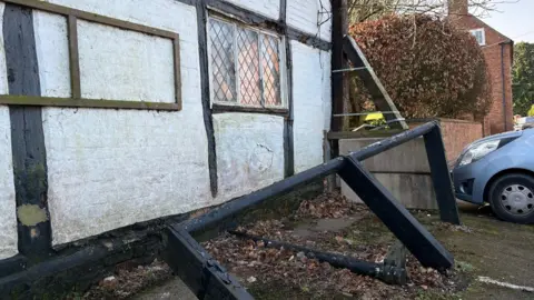 A broken, black, wooden fence sits buckled outside an empty pub.
