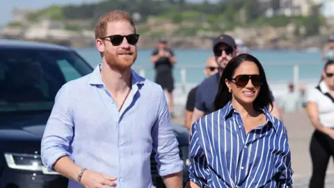 A redheaded man and a woman with dark hair walk together.