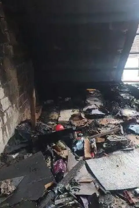 Steven Force Piles of blackened objects and rubbish in an attic, with part of the roof exposed