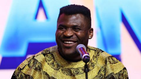 Francis Ngannou smiles broadly speaking at a news conference