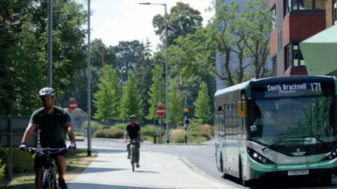 Two people cycling on bikes and a green bus on the road which reads South Bracknell.
