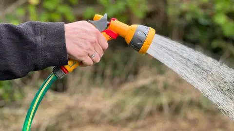 Close up of a hand holding a hosepipe gun with a shower of water coming out of the nozzle