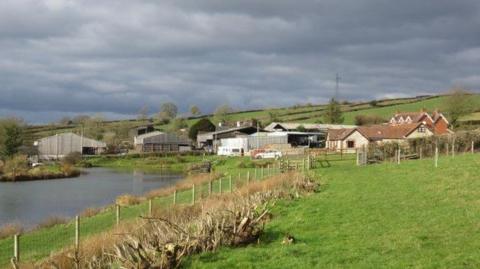 Farm building surrounded by fields and a river running alongside