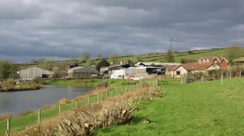 Becky Williamson Farm building surrounded by fields and a river running alongside
