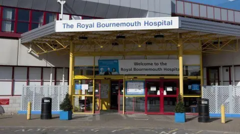 The main entrance to Royal Bournemouth Hospital is marked by blue signs on a canopy above yellow and red sliding doors.