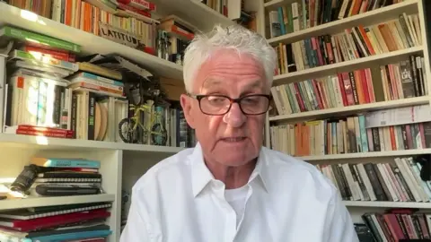 Melvin Benn in a white shirt in front of a book shelf