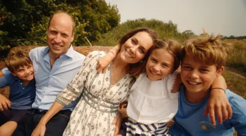 Kensington Palace Prince and Princess of Wales and their three children in a photo in front of trees and greenery in Norfolk, taken in August and used for their Christmas card.