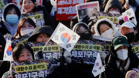 Para pengunjuk rasa EPA memegang bendera dan plakat Korea Selatan pada unjuk rasa menentang Presiden Korea Selatan yang dimakzulkan Yoon Suk Yeol, di ibu kota Seoul. 