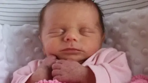 Family Darcy Leigh Jefferson, wearing a pink baby grow lying in a cot or moses basket