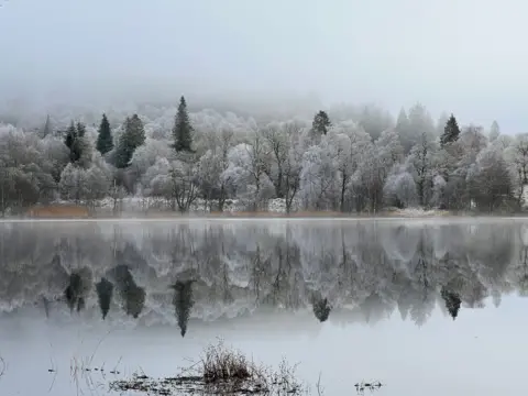 Carol Cameron Landscape of frost covered trees below a foggy sky next to a loch, mirrored in the water