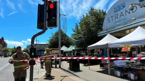 Two firemen tied red-and-white tape around lampposts outside the Strand shopping centre