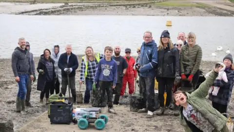 Michelle Collier A group of more than a dozen volunteers holding buckets and looking towards the camera