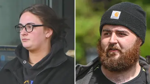 Sophie, left, wearing a black hoodie. She has black glasses and brown hair, with three earrings on her right ear. Jamie on the right has a black beanie hat on, and a large ginger beard. He is wearing a black coat