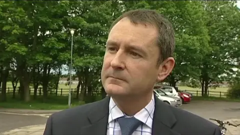 Matthew Wright is wearing a suit and looks serious as he is interviewed in a previous broadcast