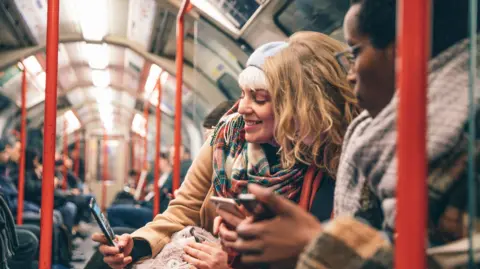 A group of friends look at phones whilst travelling on the tube