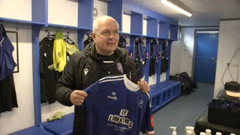 Frankie Empson, the kitman, holds up a the shirt sponsored by The Libertines, a band who have a hotel in Margate