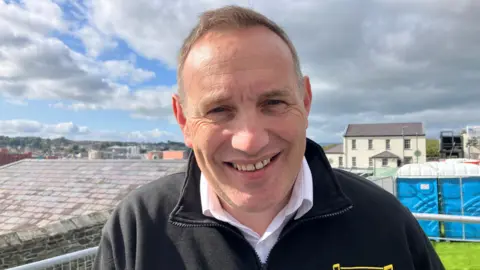 Karl Diamond. He has short brown hair, wearing a white shirt and black zip fleece.