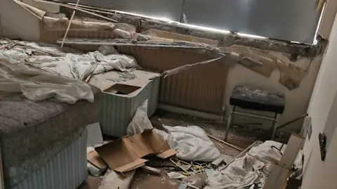 Two broken beds, one without mattress. Debris and rubbish is on the floor. It looks a mess. 