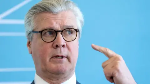 PA Media Malcolm Offord, who has grey hair and glasses, in a close-up shot in front of a blue background 