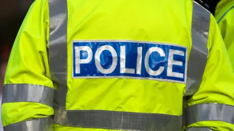 A close up of a police officer wearing a fluorescent yellow police uniform jacket.