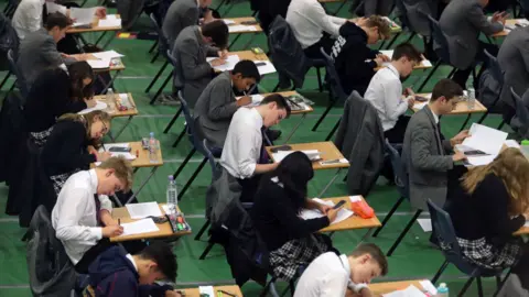 Rows of students completing an exam on desks.