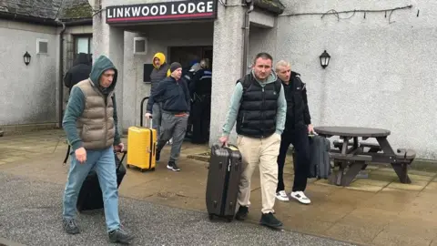 Five men leave a hotel with luggage