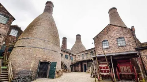 A courtyard of a former pottery, now a heritage site. Brick buildings and four bottle ovens surround the courtyard.