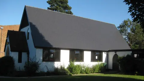 All Saints Church, South Merstham A white and black church building shrouded in shadow.