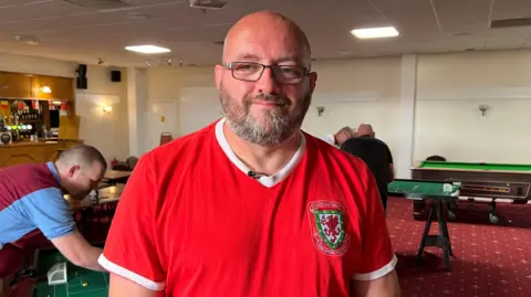 Matthew Rowley wearing red t-shirt standing in front of pool tables and bar.