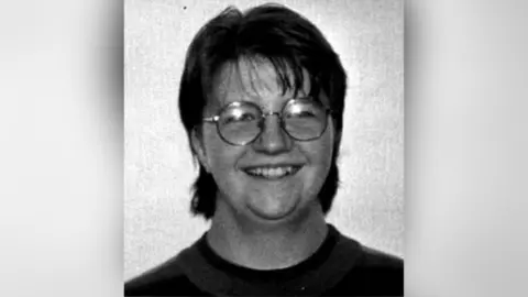 Family Handout Black and white headshot of a woman smiling at the camera wearing round glasses.