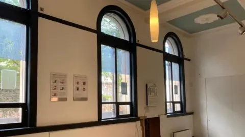 the interior of a large room with three large windows and a high ceiling