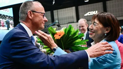 Toban Schwarz / AFP that brings a blue dressing, Merz is given a hug from his wife Charlotte (R) that brings a blue and corresponding suit