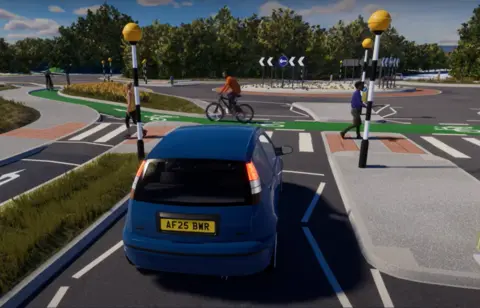 A blue car waiting at a zebra crossing as both pedestrians and a cyclist cross. There is a roundabout in the background.