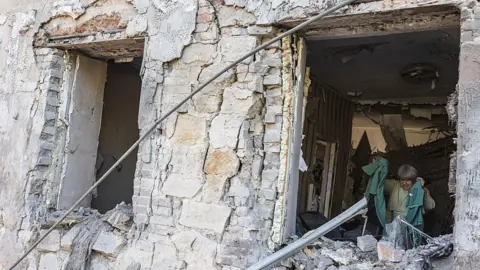 Anadolu via Getty Images An elderly woman is pictured in her home, which was badly damaged after a Russian attack on a residential building in the city of Druzhkivka, Ukraine.
