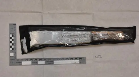 Northumbria Police A silver machete with a wooden handle, wrapped in a clear bag. The weapon is hooked at its tip. A ruled has been placed alongside the knife showing it to be about 30cm (12in) long and 10cm (94in) thick.