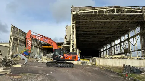 A metal structure being taken down by a JCB