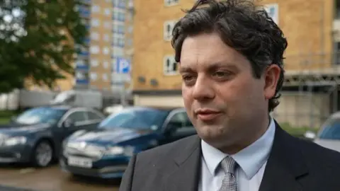 A man in a suit stood in front of cars