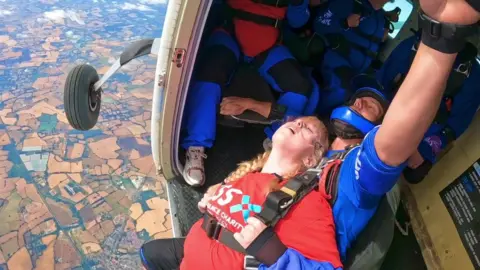 GoSkyDive A young woman with blonde hair strapped to a man in blue outfit about to jump out of a plane at height