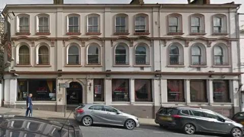 Google Three-storey building with many windows on a sloping street