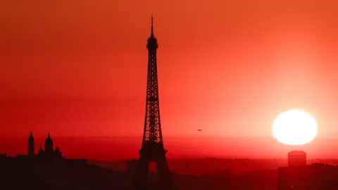 Getty Images The sun rises by the Eiffel Tower in Paris as the city is on red alert for high temperatures, with the top of the Eiffel Tower shut