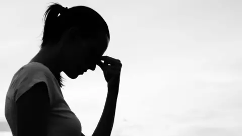 A silhouette of a woman, resting her fingers to her forehead, possibly in pain.