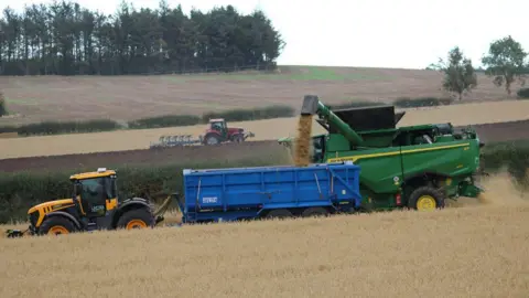 Christopher Heap Two tractors head in different directions - one of them large in the foreground and the other more distant.