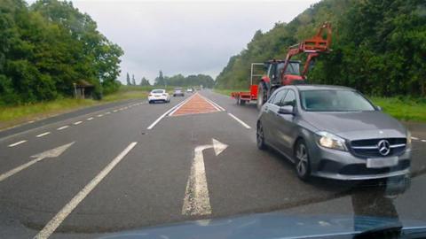 Silver car overtaking a tractor next to a right-hand turning lane